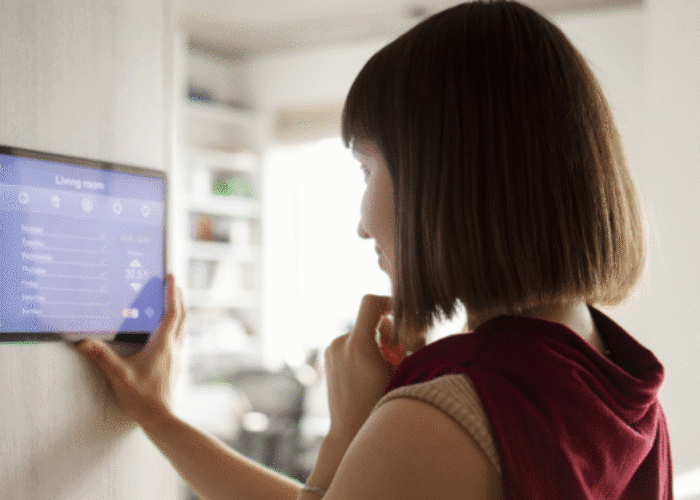 Woman controlling a whole home or multi-room audio system by pressing room locations on a wall mounted touchscreen tablet.