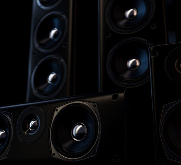 Multiple large sleek black speakers with chrome centers enhanced by accent lighting in a dark room.