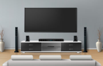Beautiful living room with big flat screen TV on flat gray wall, entertainment cabinet with modern home theater speaker system with white sofa for watching movies.